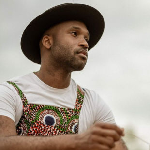 The artist wearing a patchwork dungaree over a white t-shirt, holding cottongrass.