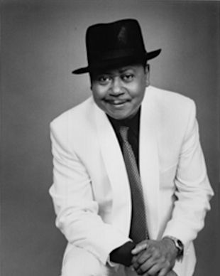 Old style black and white photo. The musician wearing white jacket, black hat, black shirt and a tie